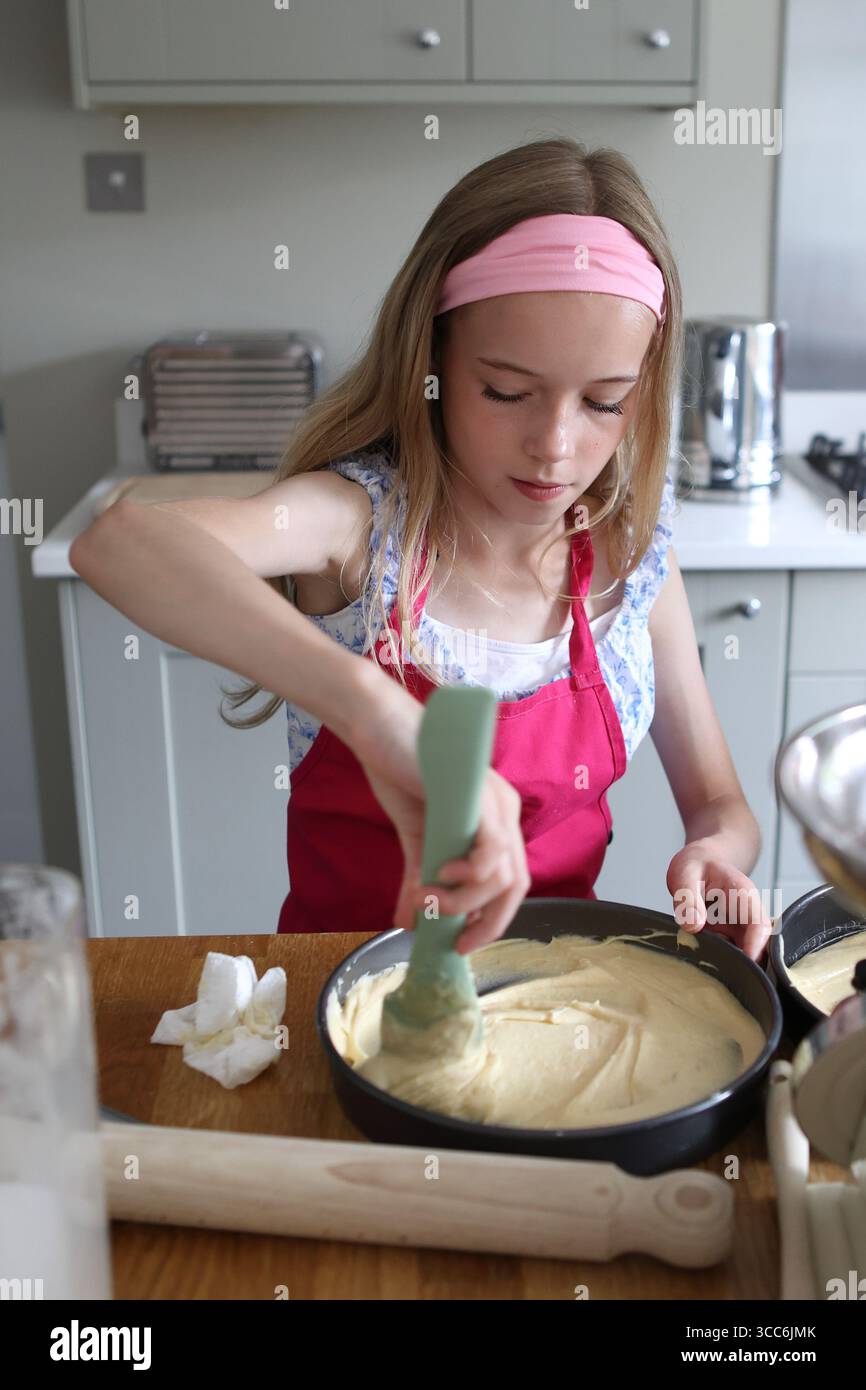 Mädchen backt Kuchen in der Küche und verteilt Kuchenmischung in Backform Stockfoto
