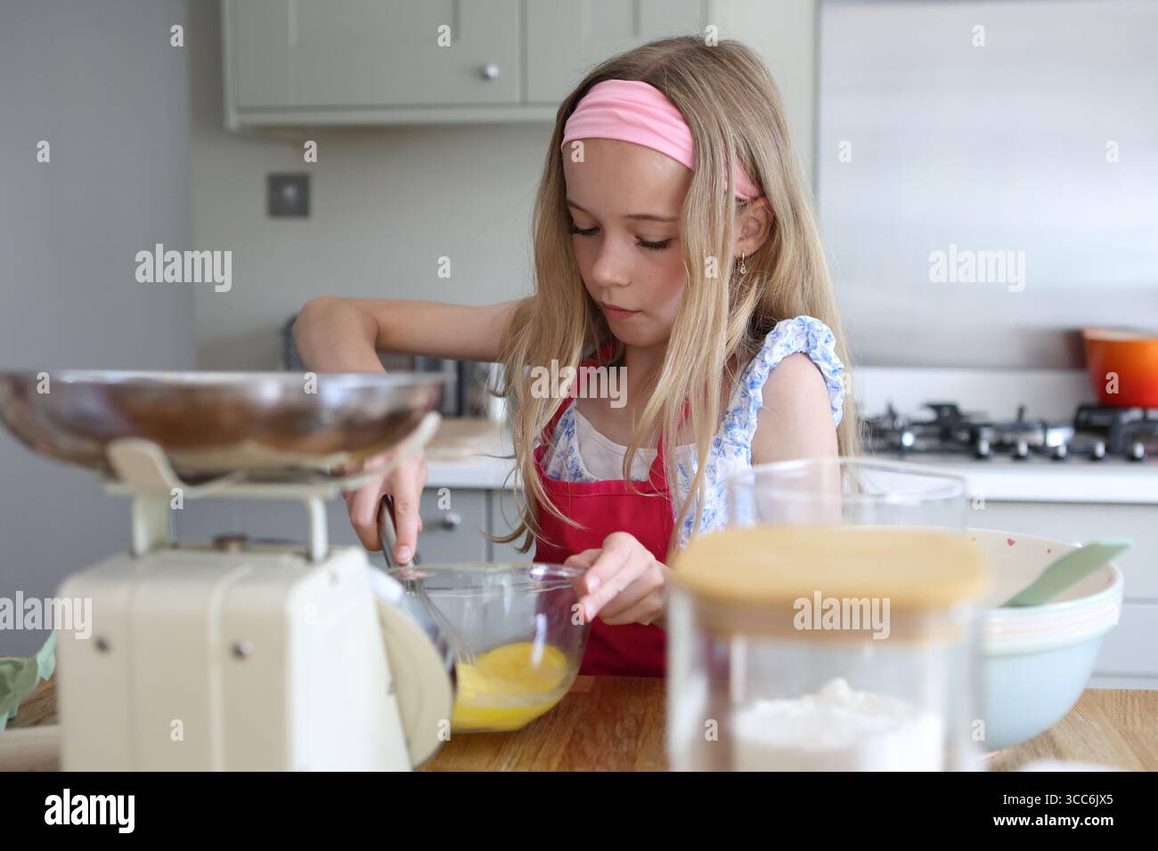 Mädchen, das Eier zum Backen von Kuchen in der Küchenschüssel mit dem Handrührer verquirlt Stockfoto