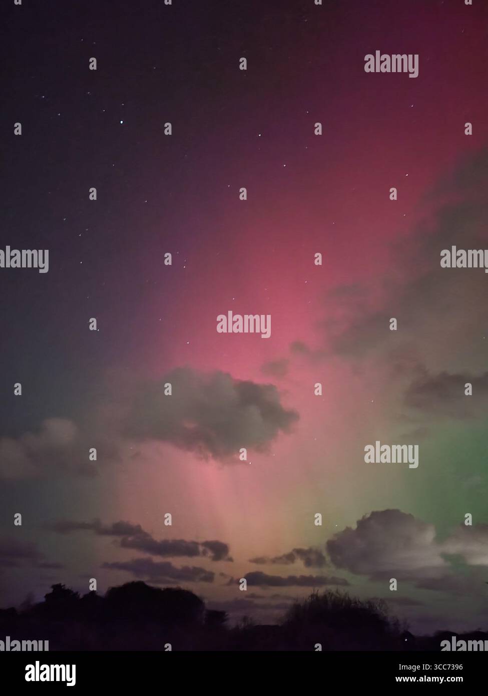 Leuchtend rosa und grüne aurora Borealis, die den Nachthimmel über Wolken und Landschaft erleuchten. - Smartphone-aufgenommenes Stockfoto