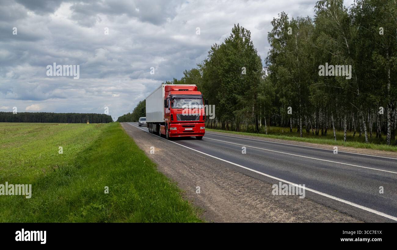 Roter Lkw fährt im Sommer auf der Autobahn durch Waldlandschaft und Feld. Stockfoto