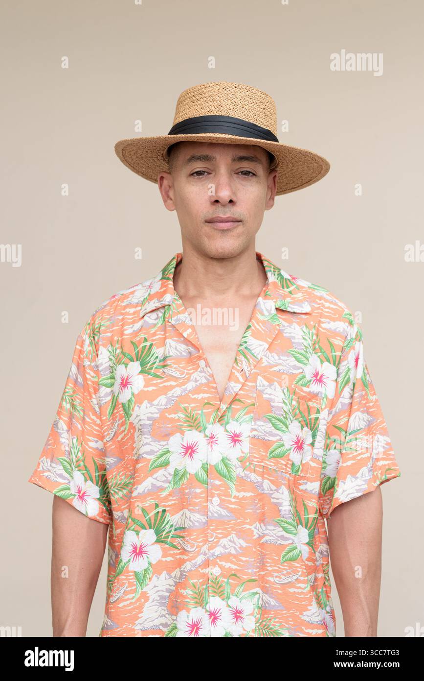 Glücklicher hispanischer Mann mit Panamahut und tropischem hawaiianischem Hemd, gekleidet in legere Sommermode. Der fröhliche Tourist posiert in entspanntem Urlaub Stockfoto