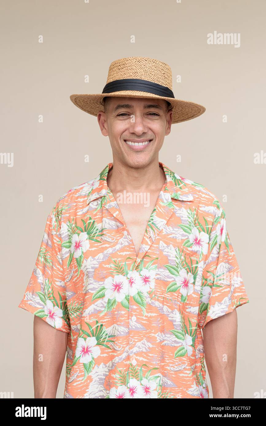 Glücklicher hispanischer Mann mit Panamahut und tropischem hawaiianischem Hemd, gekleidet in legere Sommermode. Der fröhliche Tourist posiert in entspanntem Urlaub Stockfoto