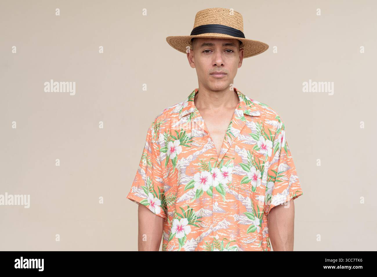 Glücklicher hispanischer Mann mit Panamahut und tropischem hawaiianischem Hemd, gekleidet in legere Sommermode. Der fröhliche Tourist posiert in entspanntem Urlaub Stockfoto