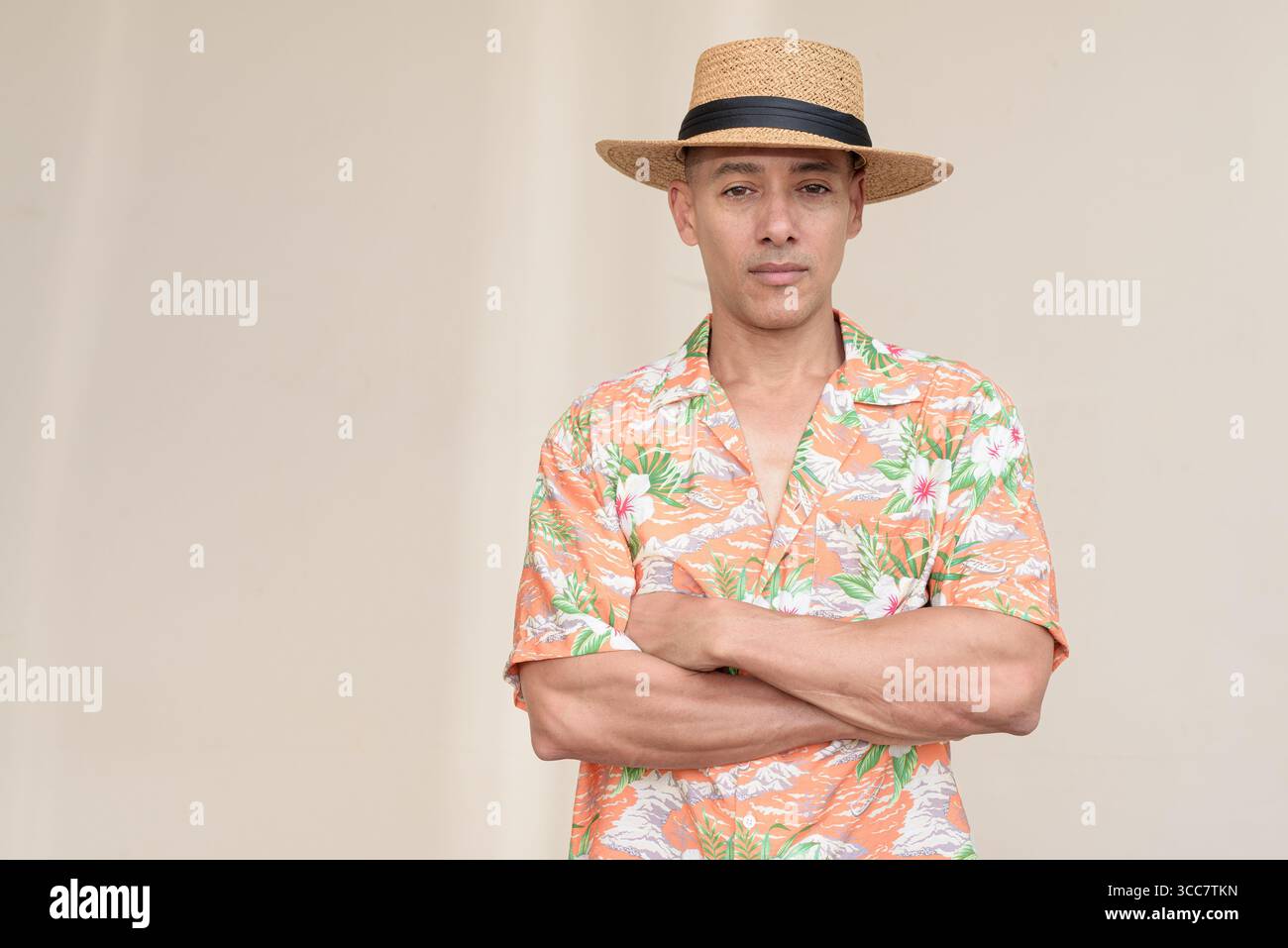 Glücklicher hispanischer Mann mit Panamahut und tropischem hawaiianischem Hemd, gekleidet in legere Sommermode. Der fröhliche Tourist posiert in entspanntem Urlaub Stockfoto