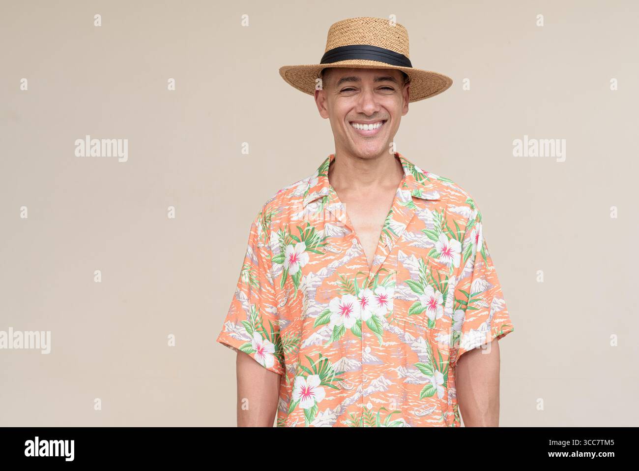 Glücklicher hispanischer Mann mit Panamahut und tropischem hawaiianischem Hemd, gekleidet in legere Sommermode. Der fröhliche Tourist posiert in entspanntem Urlaub Stockfoto
