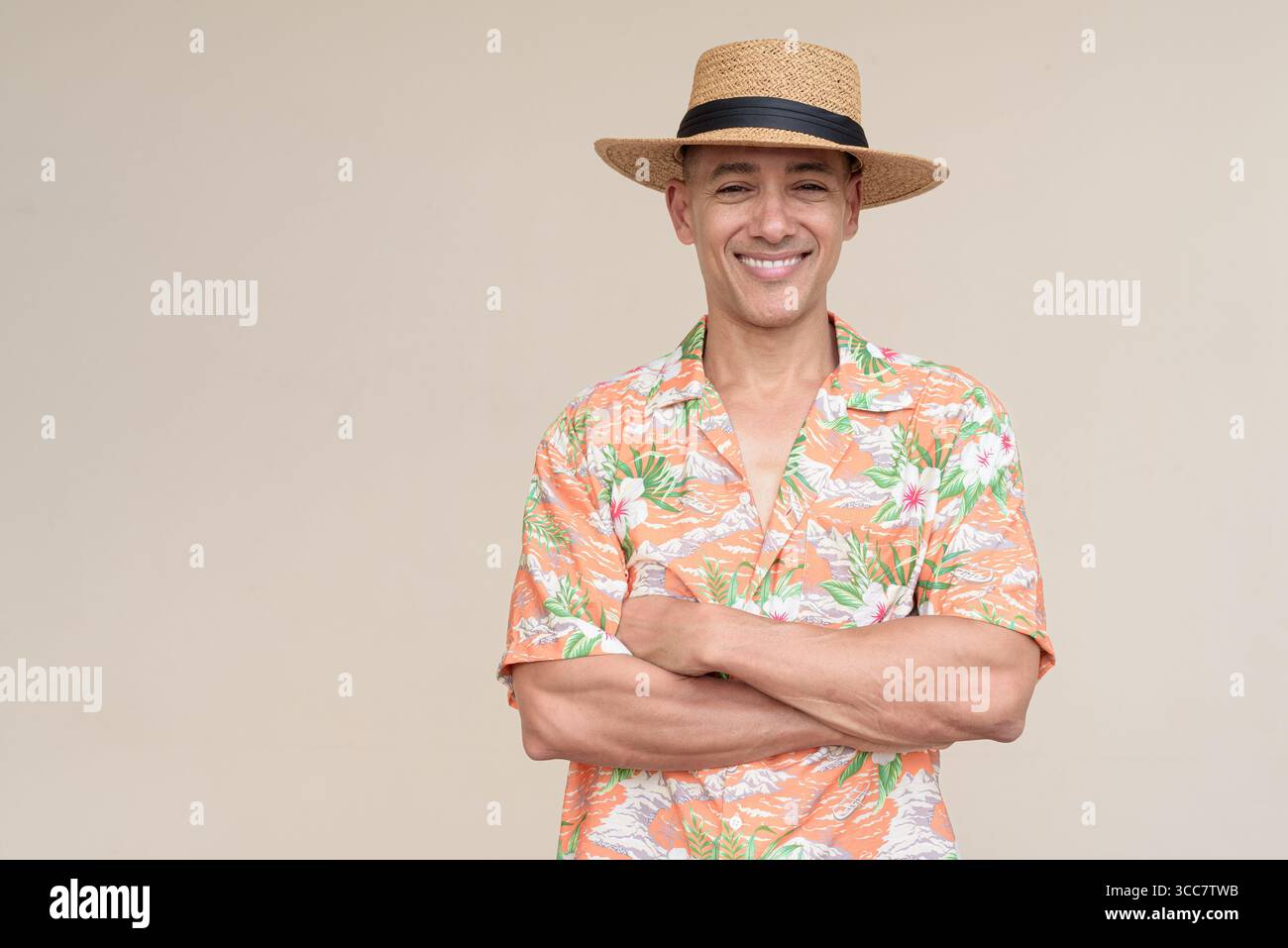 Glücklicher hispanischer Mann mit Panamahut und tropischem hawaiianischem Hemd, gekleidet in legere Sommermode. Der fröhliche Tourist posiert in entspanntem Urlaub Stockfoto