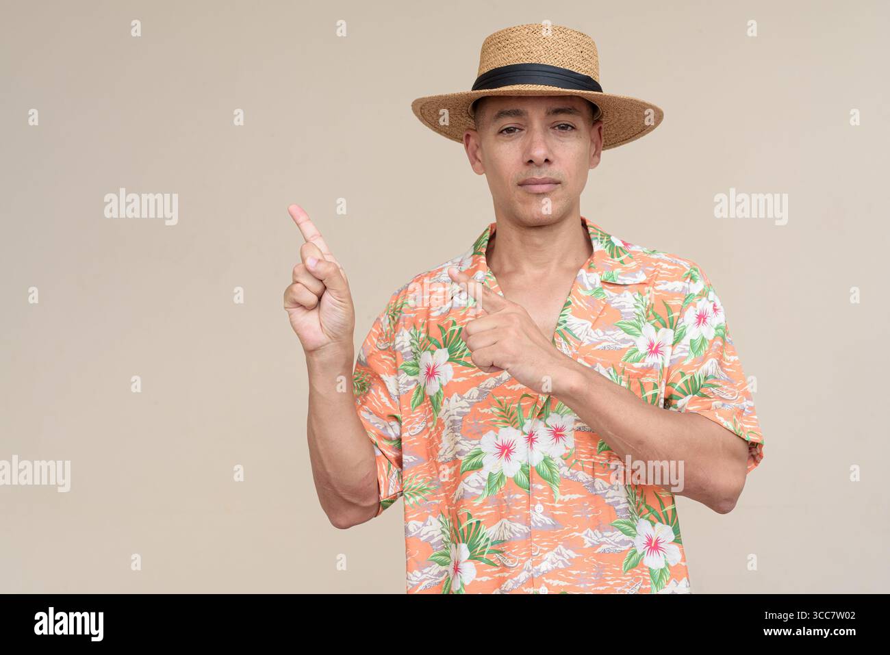 Glücklicher hispanischer Mann mit Panamahut und tropischem hawaiianischem Hemd, gekleidet in legere Sommermode. Der fröhliche Tourist posiert in entspanntem Urlaub Stockfoto