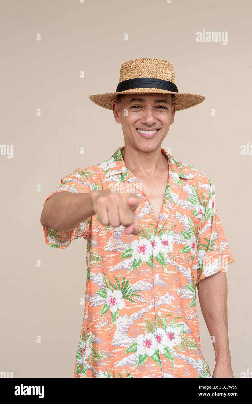 Glücklicher hispanischer Mann mit Panamahut und tropischem hawaiianischem Hemd, gekleidet in legere Sommermode. Der fröhliche Tourist posiert in entspanntem Urlaub Stockfoto