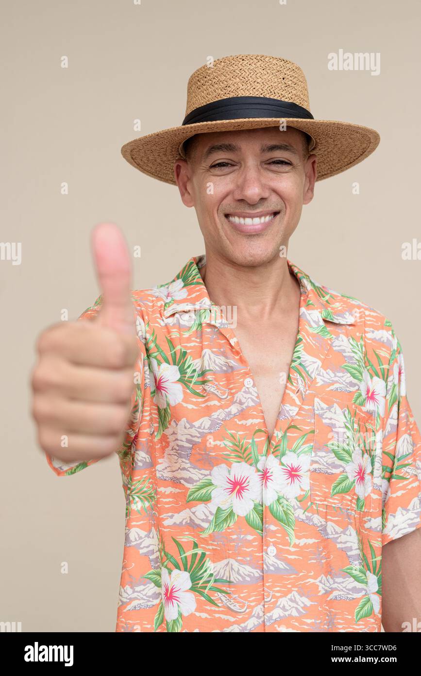 Glücklicher hispanischer Mann mit Panamahut und tropischem hawaiianischem Hemd, gekleidet in legere Sommermode. Der fröhliche Tourist posiert in entspanntem Urlaub Stockfoto