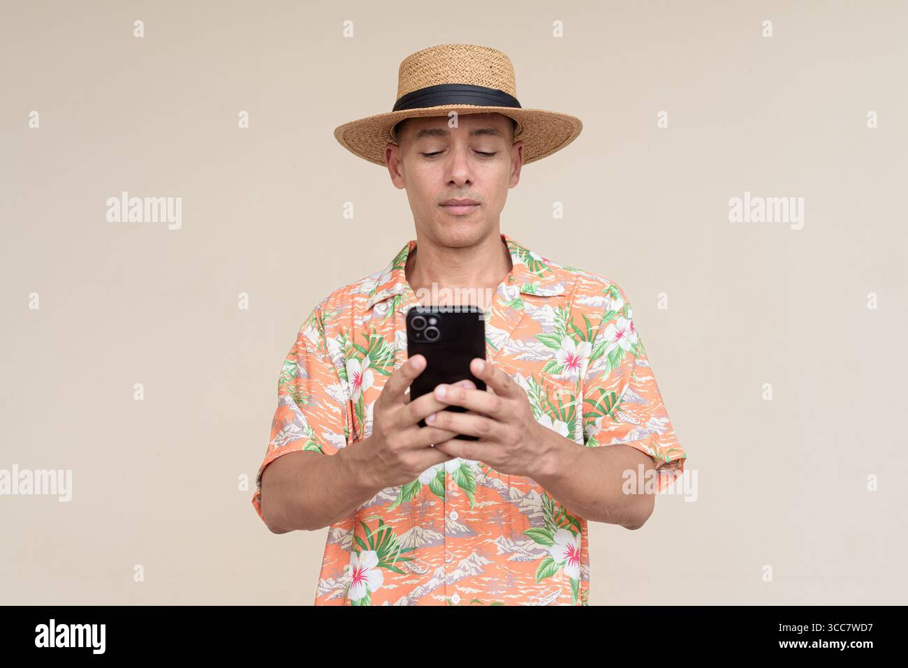 Glücklicher hispanischer Mann mit Panamahut und tropischem hawaiianischem Hemd, gekleidet in legere Sommermode. Der fröhliche Tourist posiert in entspanntem Urlaub Stockfoto