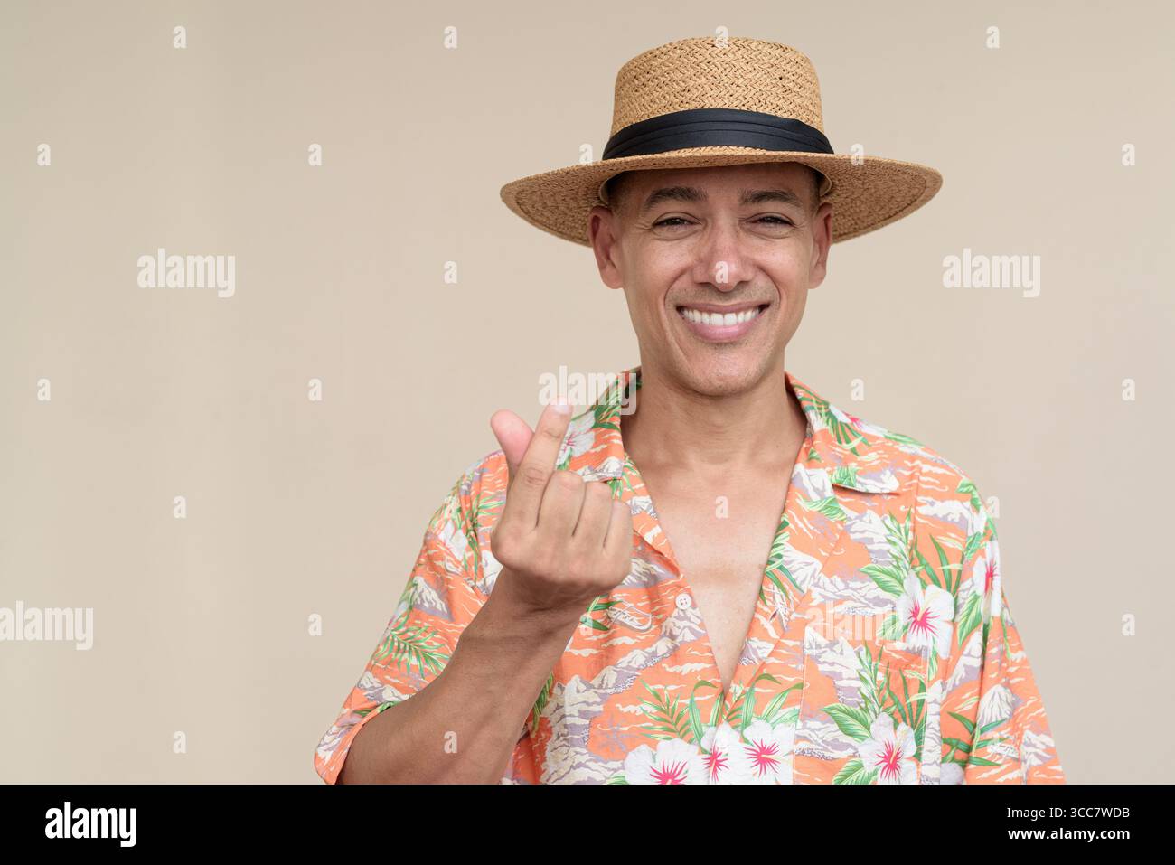 Glücklicher hispanischer Mann mit Panamahut und tropischem hawaiianischem Hemd, gekleidet in legere Sommermode. Der fröhliche Tourist posiert in entspanntem Urlaub Stockfoto