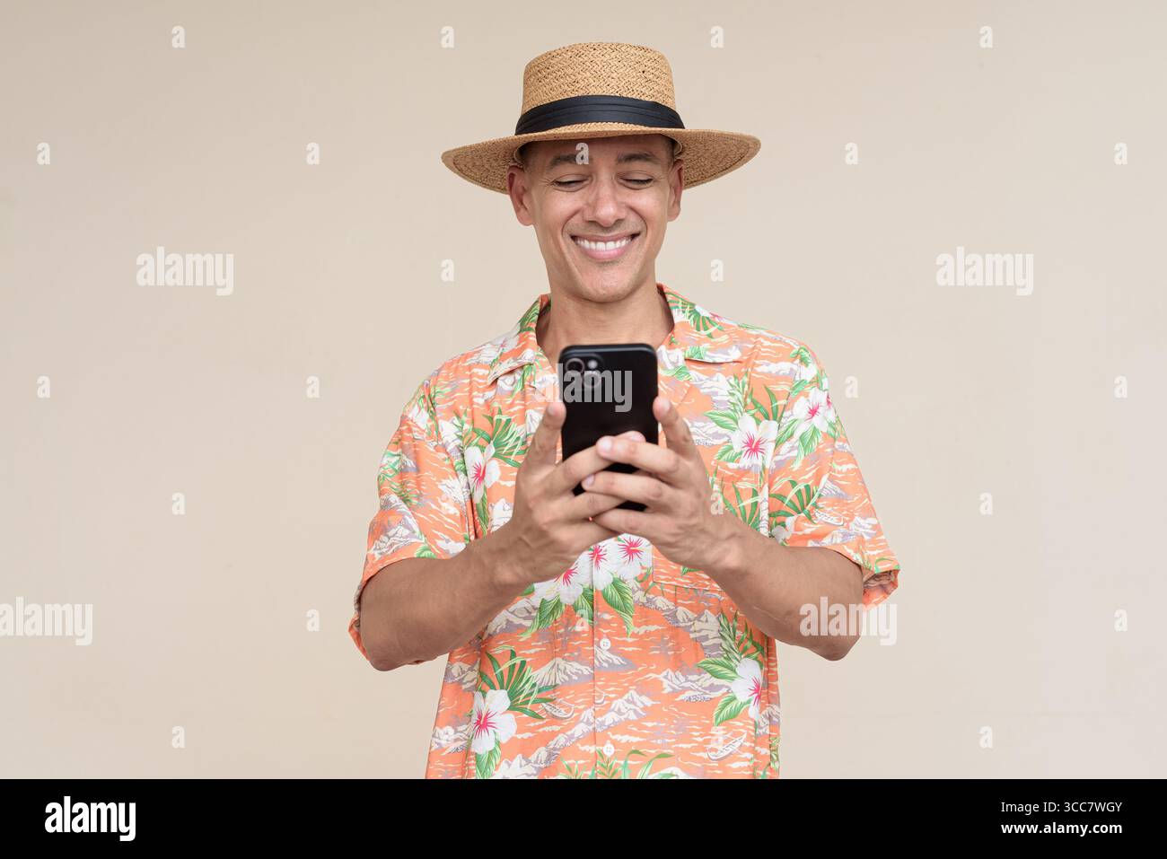 Glücklicher hispanischer Mann mit Panamahut und tropischem hawaiianischem Hemd, gekleidet in legere Sommermode. Der fröhliche Tourist posiert in entspanntem Urlaub Stockfoto