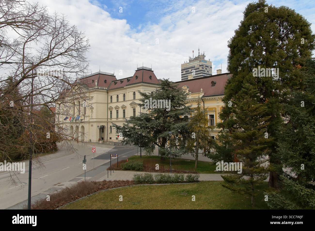 Die elegante Fassade eines Gebäudes wird von Bäumen unter bewölktem Himmel eingerahmt und bietet einen ruhigen Blick auf Veszprém, Ungarn. Stockfoto
