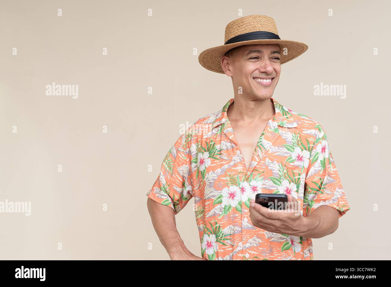 Glücklicher hispanischer Mann mit Panamahut und tropischem hawaiianischem Hemd, gekleidet in legere Sommermode. Der fröhliche Tourist posiert in entspanntem Urlaub Stockfoto