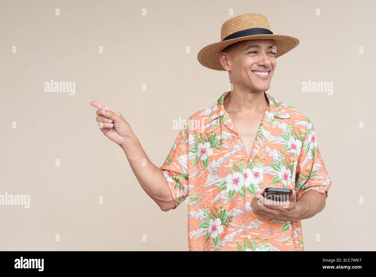 Glücklicher hispanischer Mann mit Panamahut und tropischem hawaiianischem Hemd, gekleidet in legere Sommermode. Der fröhliche Tourist posiert in entspanntem Urlaub Stockfoto