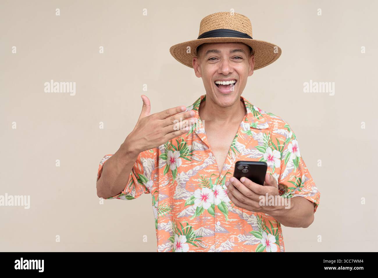 Glücklicher hispanischer Mann mit Panamahut und tropischem hawaiianischem Hemd, gekleidet in legere Sommermode. Der fröhliche Tourist posiert in entspanntem Urlaub Stockfoto