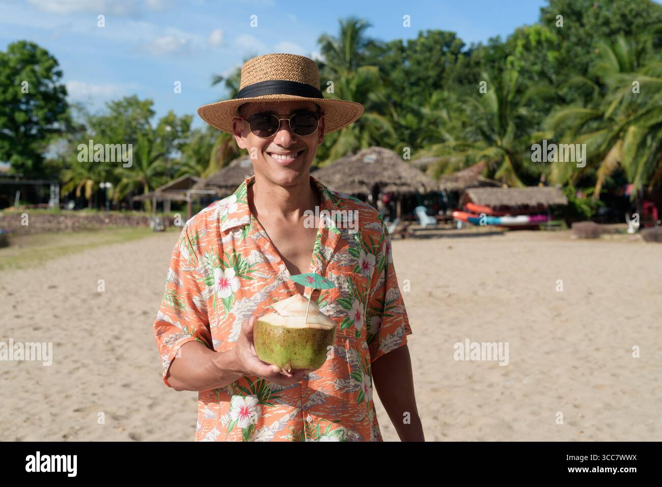 Hispanischer Mann mit Panamahut und hawaiianischem Hemd, gekleidet im lässigen Sommerurlaub-Stil. Er posiert am Strand und zeigt eine entspannte Urlaubsatmosphäre Stockfoto