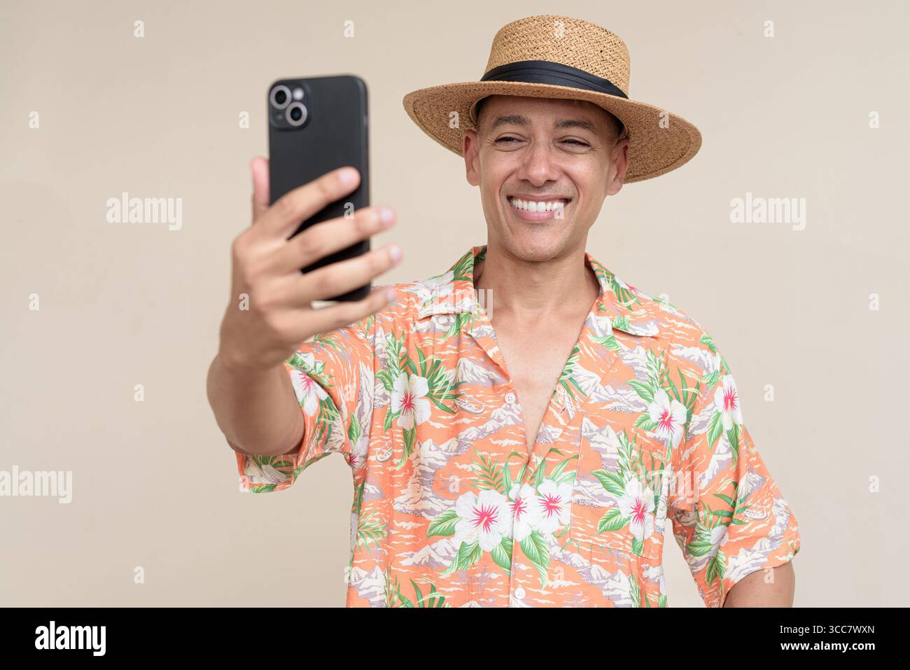 Glücklicher hispanischer Mann mit Panamahut und tropischem hawaiianischem Hemd, gekleidet in legere Sommermode. Der fröhliche Tourist posiert in entspanntem Urlaub Stockfoto