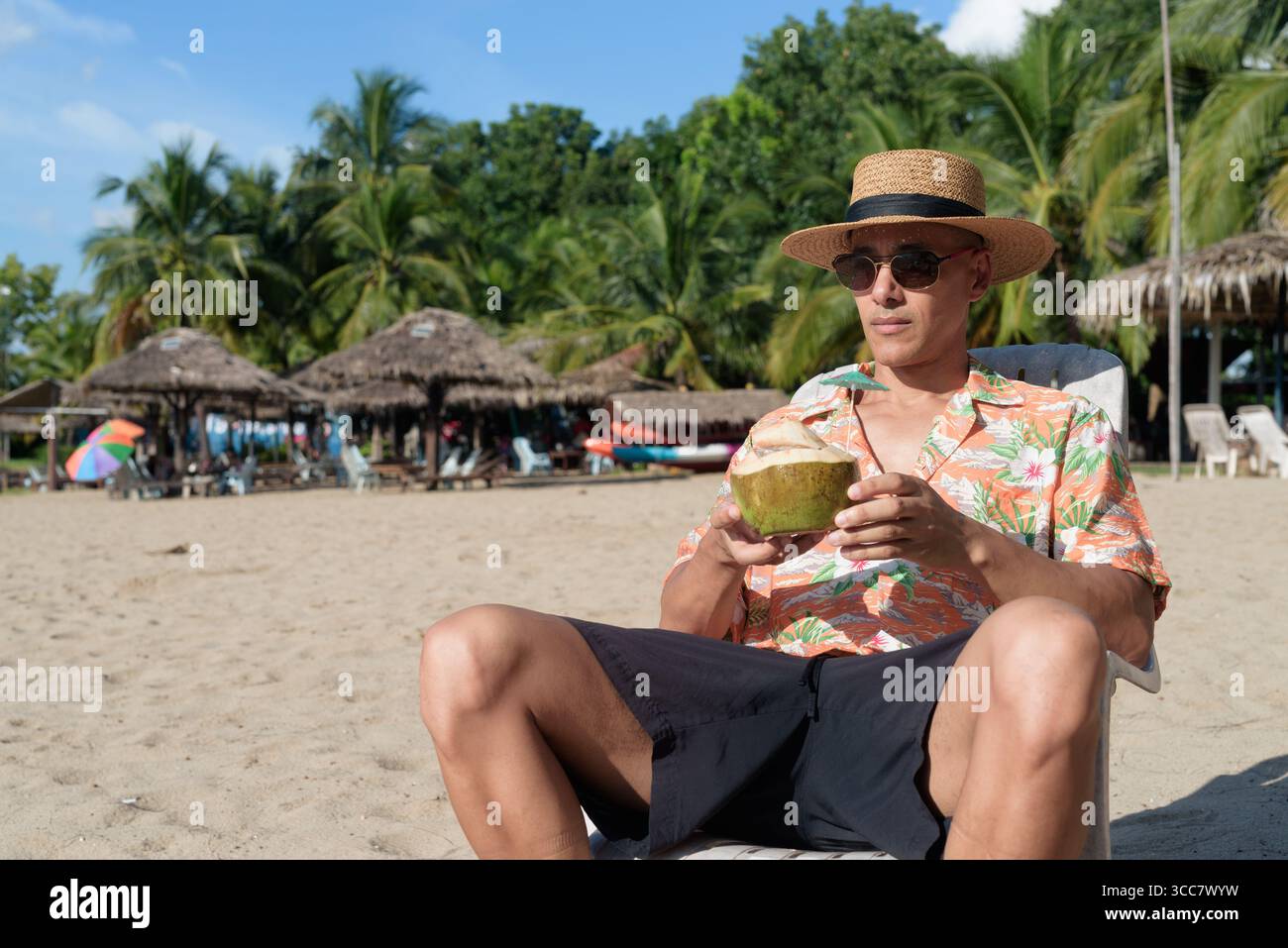 Hispanischer Mann mit Panamahut und hawaiianischem Hemd, gekleidet im lässigen Sommerurlaub-Stil. Er posiert am Strand und zeigt eine entspannte Urlaubsatmosphäre Stockfoto