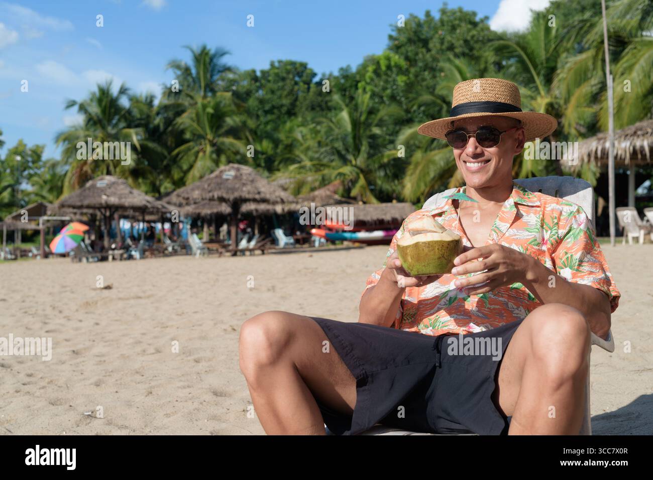 Hispanischer Mann mit Panamahut und hawaiianischem Hemd, gekleidet im lässigen Sommerurlaub-Stil. Er posiert am Strand und zeigt eine entspannte Urlaubsatmosphäre Stockfoto