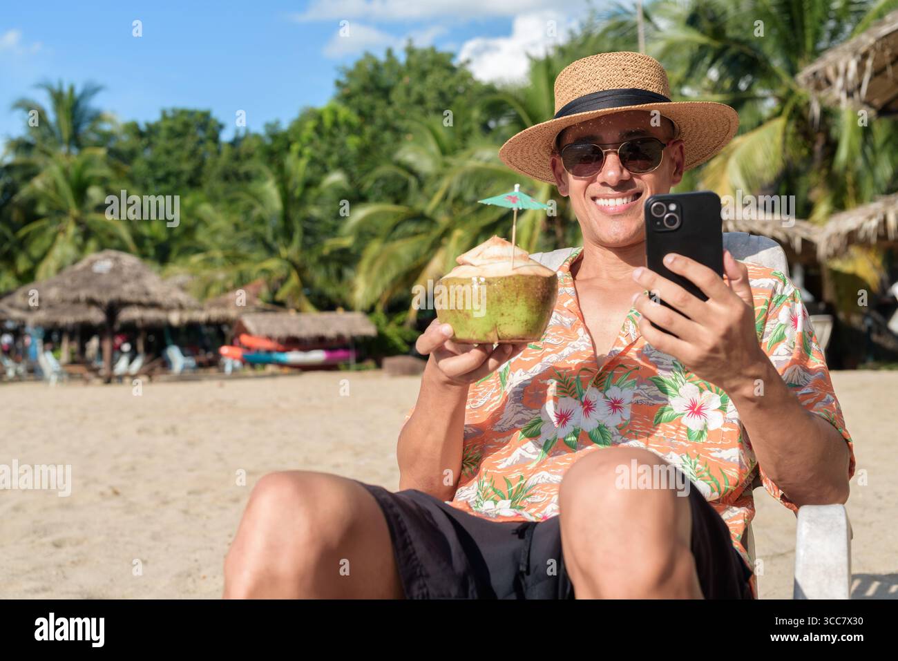Hispanischer Mann mit Panamahut und hawaiianischem Hemd, gekleidet im lässigen Sommerurlaub-Stil. Er posiert am Strand und zeigt eine entspannte Urlaubsatmosphäre Stockfoto