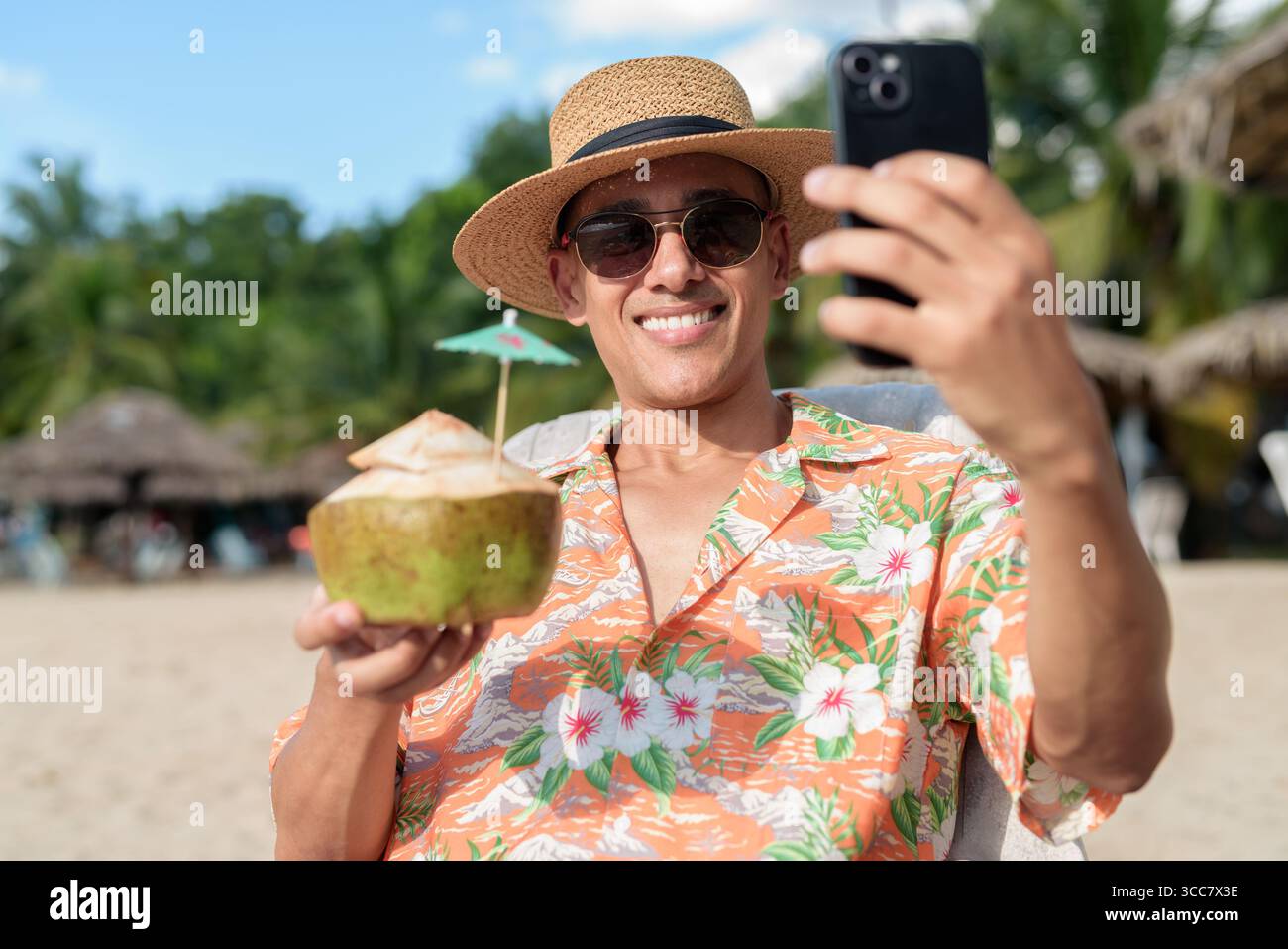 Hispanischer Mann mit Panamahut und hawaiianischem Hemd, gekleidet im lässigen Sommerurlaub-Stil. Er posiert am Strand und zeigt eine entspannte Urlaubsatmosphäre Stockfoto
