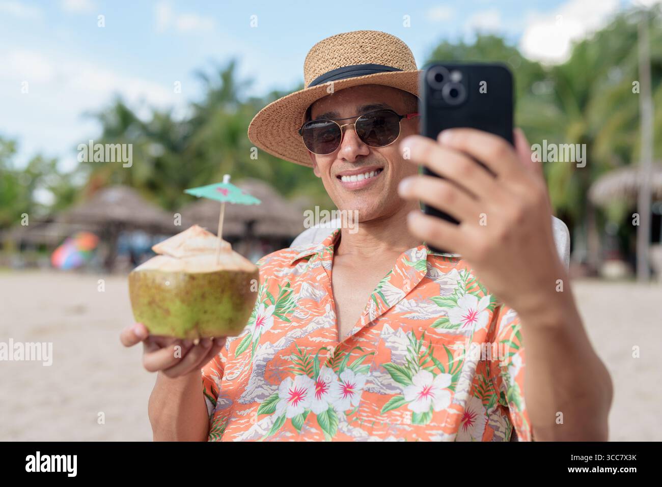 Hispanischer Mann mit Panamahut und hawaiianischem Hemd, gekleidet im lässigen Sommerurlaub-Stil. Er posiert am Strand und zeigt eine entspannte Urlaubsatmosphäre Stockfoto