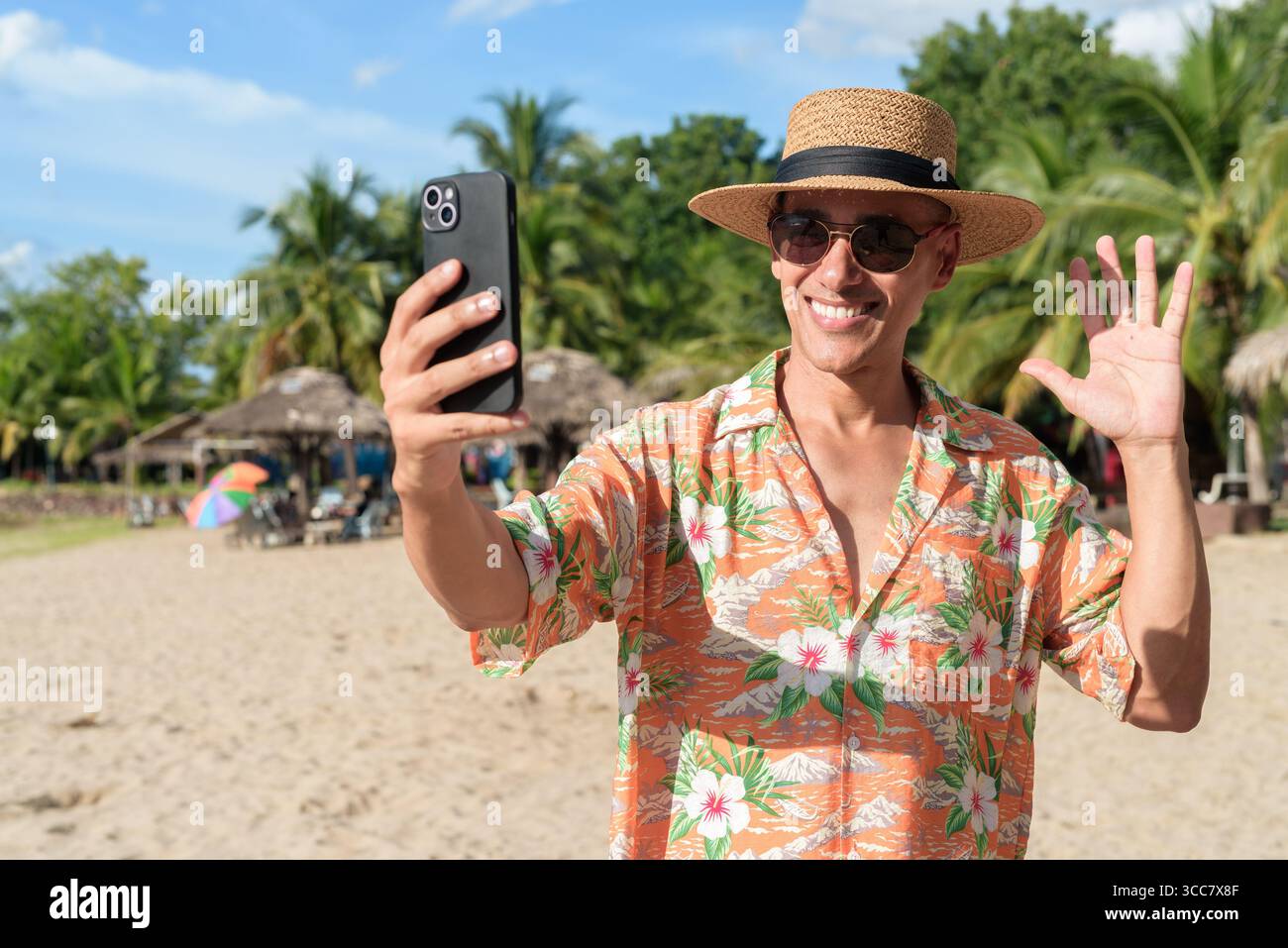 Hispanischer Mann mit Panamahut und hawaiianischem Hemd, gekleidet im lässigen Sommerurlaub-Stil. Er posiert am Strand und zeigt eine entspannte Urlaubsatmosphäre Stockfoto