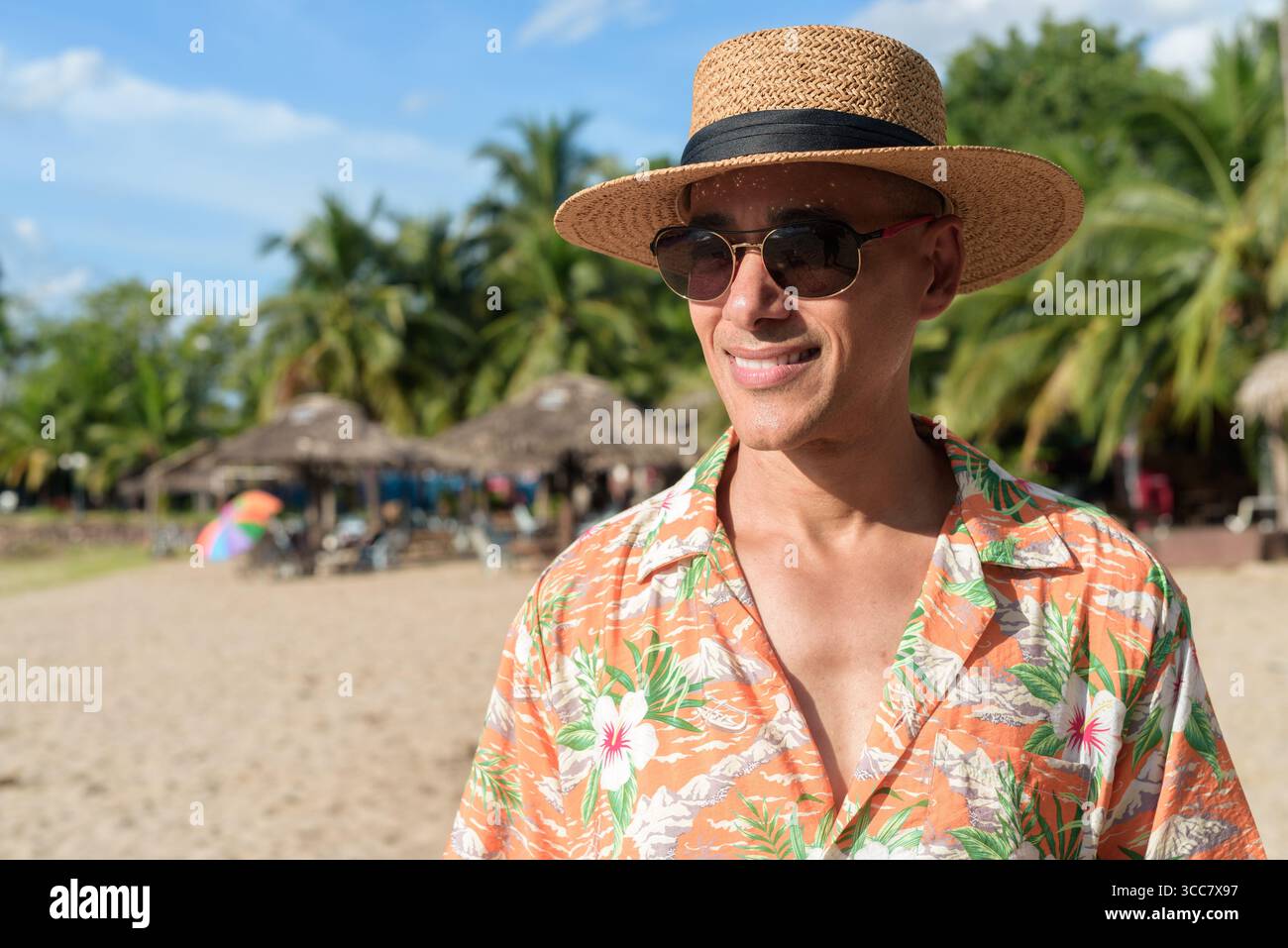 Hispanischer Mann mit Panamahut und hawaiianischem Hemd, gekleidet im lässigen Sommerurlaub-Stil. Er posiert am Strand und zeigt eine entspannte Urlaubsatmosphäre Stockfoto