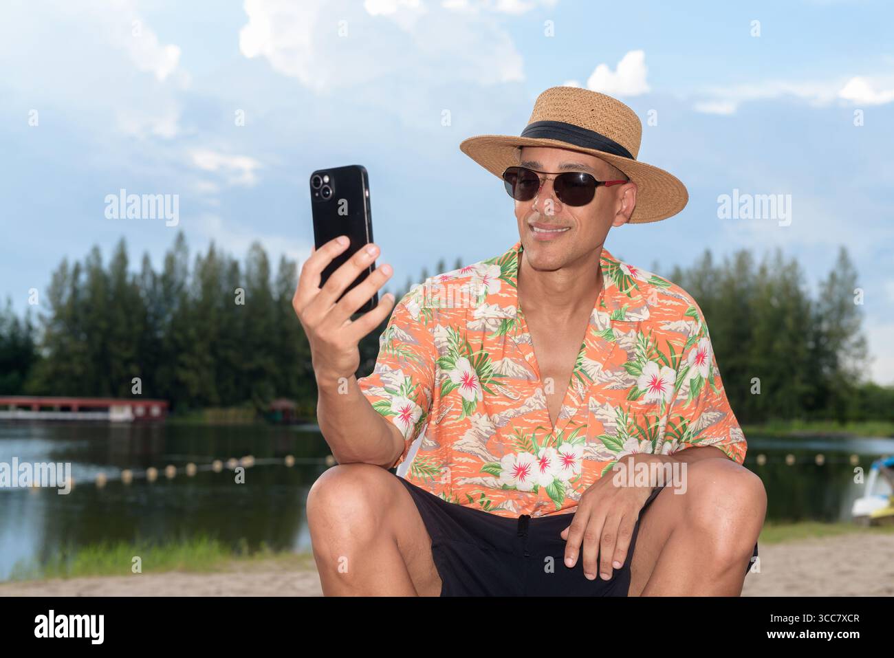 Hispanischer Mann mit Panamahut und hawaiianischem Hemd, gekleidet im lässigen Sommerurlaub-Stil. Er posiert am Strand und zeigt eine entspannte Urlaubsatmosphäre Stockfoto
