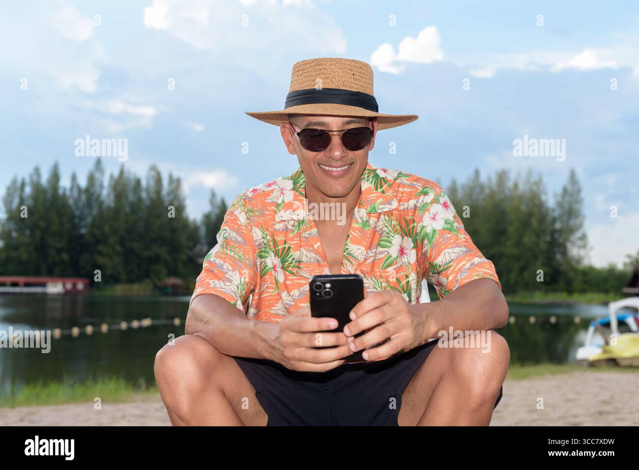Hispanischer Mann mit Panamahut und hawaiianischem Hemd, gekleidet im lässigen Sommerurlaub-Stil. Er posiert am Strand und zeigt eine entspannte Urlaubsatmosphäre Stockfoto