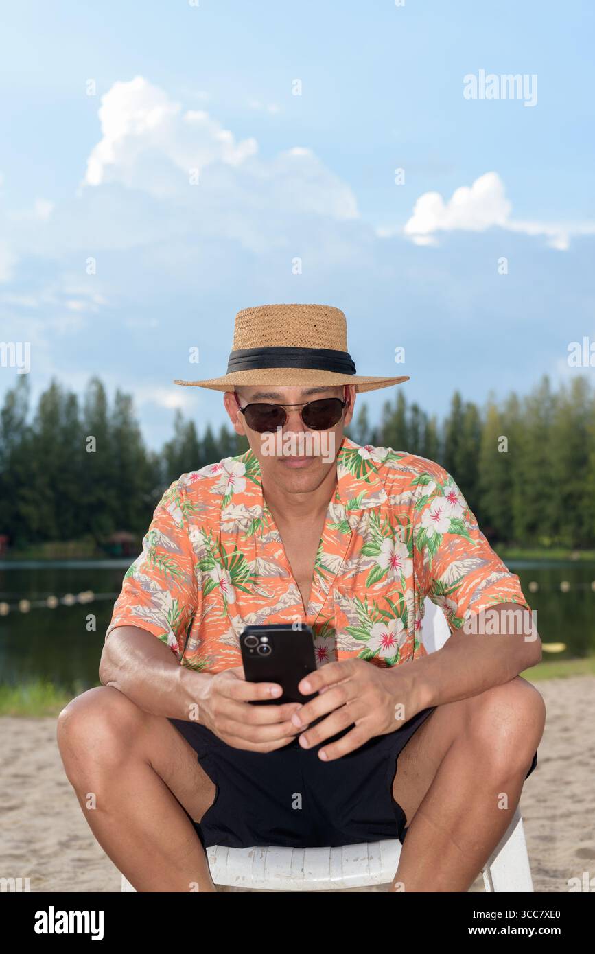 Hispanischer Mann mit Panamahut und hawaiianischem Hemd, gekleidet im lässigen Sommerurlaub-Stil. Er posiert am Strand und zeigt eine entspannte Urlaubsatmosphäre Stockfoto
