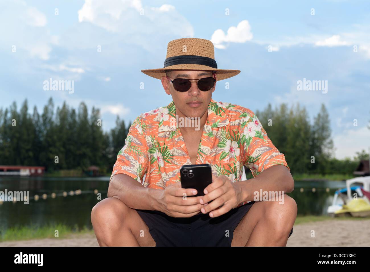 Hispanischer Mann mit Panamahut und hawaiianischem Hemd, gekleidet im lässigen Sommerurlaub-Stil. Er posiert am Strand und zeigt eine entspannte Urlaubsatmosphäre Stockfoto