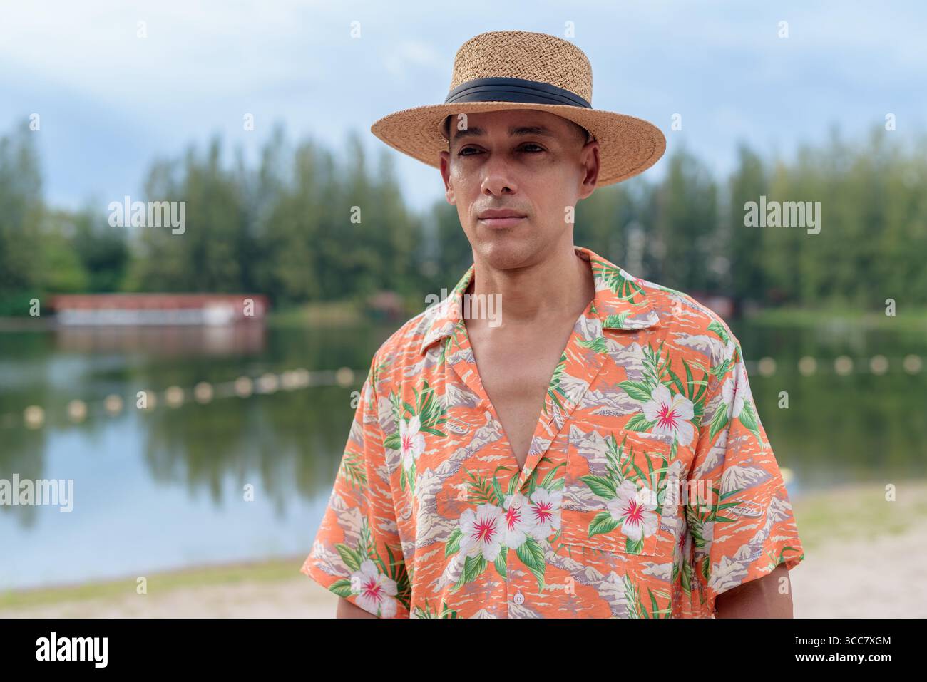 Hispanischer Mann mit Panamahut und hawaiianischem Hemd, gekleidet im lässigen Sommerurlaub-Stil. Er posiert am Strand und zeigt eine entspannte Urlaubsatmosphäre Stockfoto