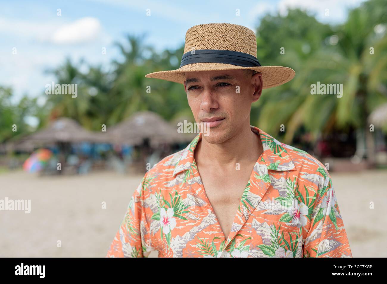 Hispanischer Mann mit Panamahut und hawaiianischem Hemd, gekleidet im lässigen Sommerurlaub-Stil. Er posiert am Strand und zeigt eine entspannte Urlaubsatmosphäre Stockfoto