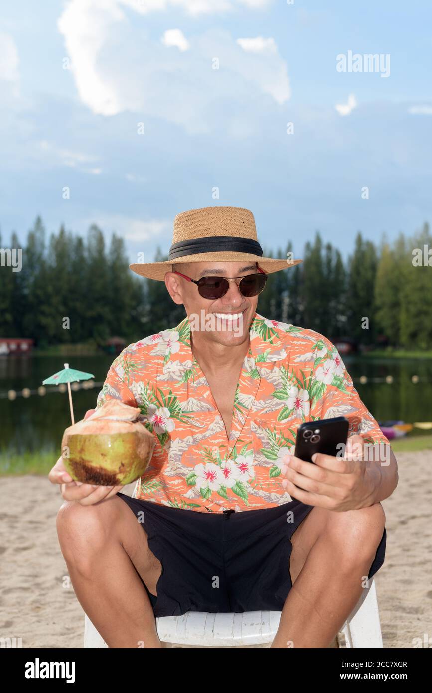 Hispanischer Mann mit Panamahut und hawaiianischem Hemd, gekleidet im lässigen Sommerurlaub-Stil. Er posiert am Strand und zeigt eine entspannte Urlaubsatmosphäre Stockfoto