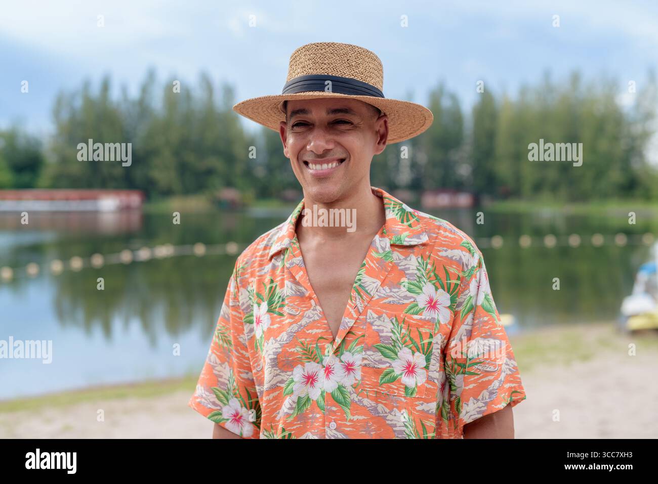 Hispanischer Mann mit Panamahut und hawaiianischem Hemd, gekleidet im lässigen Sommerurlaub-Stil. Er posiert am Strand und zeigt eine entspannte Urlaubsatmosphäre Stockfoto