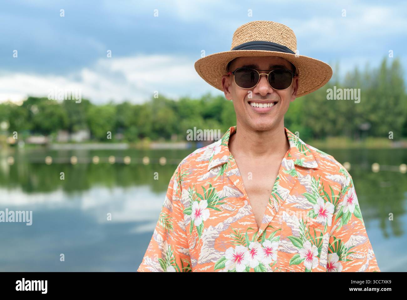 Hispanischer Mann mit Panamahut und hawaiianischem Hemd, gekleidet im lässigen Sommerurlaub-Stil. Er posiert am Strand und zeigt eine entspannte Urlaubsatmosphäre Stockfoto