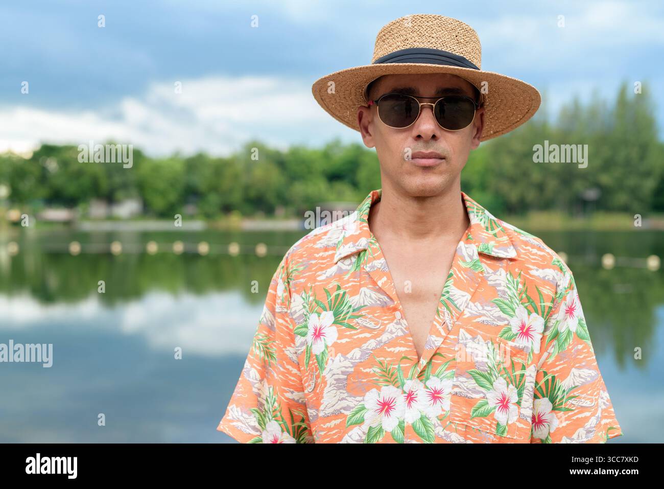 Hispanischer Mann mit Panamahut und hawaiianischem Hemd, gekleidet im lässigen Sommerurlaub-Stil. Er posiert am Strand und zeigt eine entspannte Urlaubsatmosphäre Stockfoto