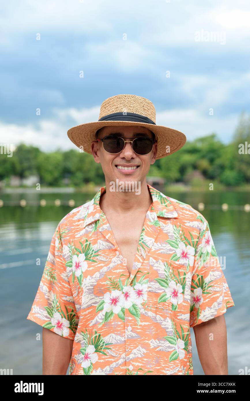 Hispanischer Mann mit Panamahut und hawaiianischem Hemd, gekleidet im lässigen Sommerurlaub-Stil. Er posiert am Strand und zeigt eine entspannte Urlaubsatmosphäre Stockfoto