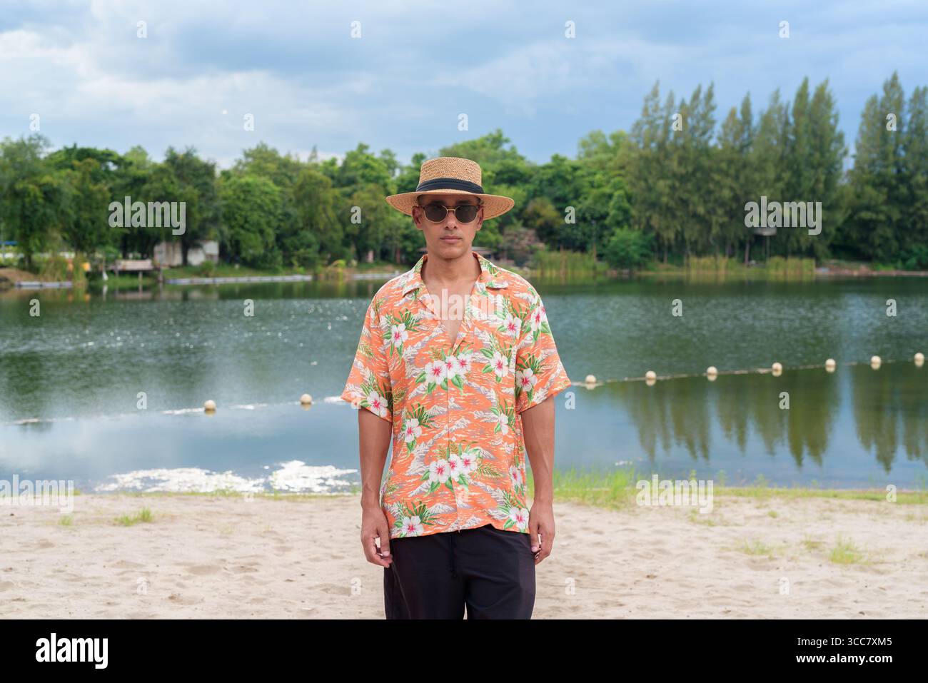 Hispanischer Mann mit Panamahut und hawaiianischem Hemd, gekleidet im lässigen Sommerurlaub-Stil. Er posiert am Strand und zeigt eine entspannte Urlaubsatmosphäre Stockfoto