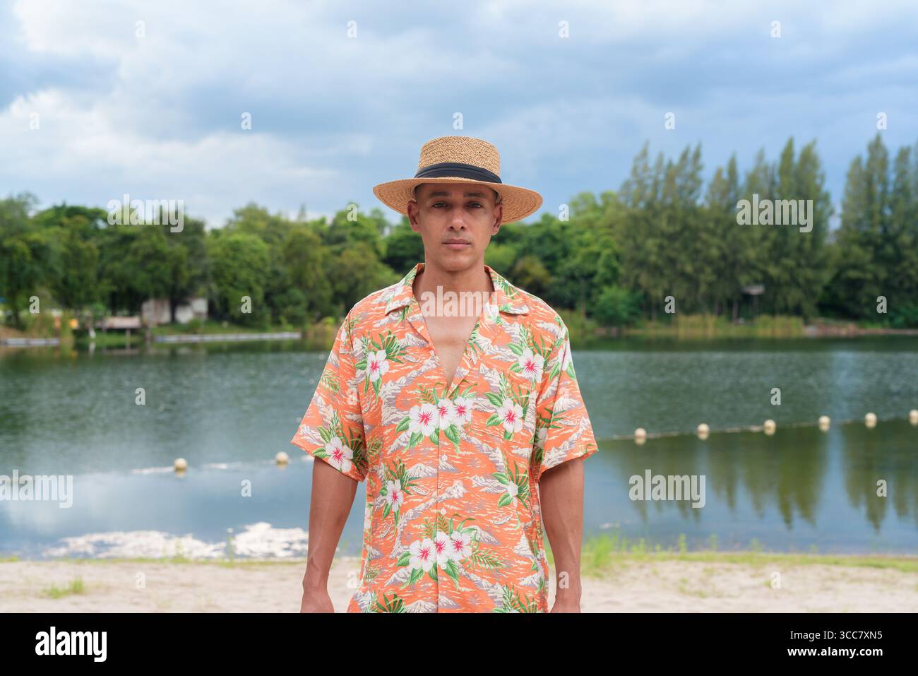 Hispanischer Mann mit Panamahut und hawaiianischem Hemd, gekleidet im lässigen Sommerurlaub-Stil. Er posiert am Strand und zeigt eine entspannte Urlaubsatmosphäre Stockfoto
