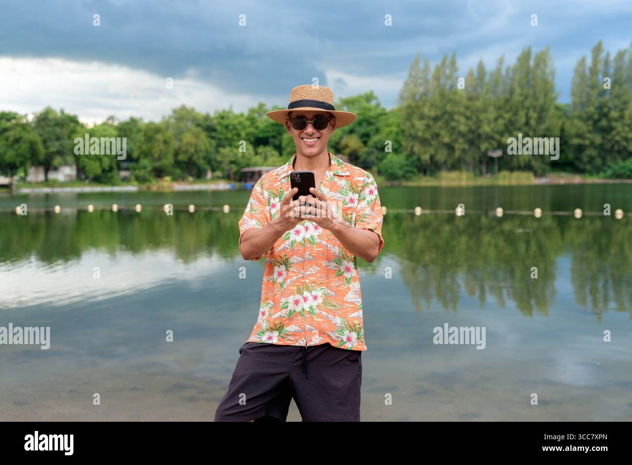 Hispanischer Mann mit Panamahut und hawaiianischem Hemd, gekleidet im lässigen Sommerurlaub-Stil. Er posiert am Strand und zeigt eine entspannte Urlaubsatmosphäre Stockfoto