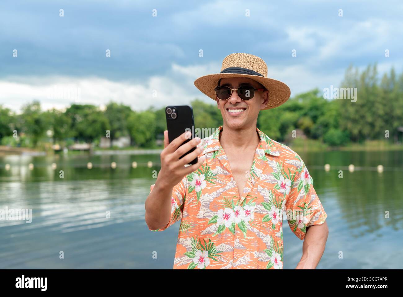 Hispanischer Mann mit Panamahut und hawaiianischem Hemd, gekleidet im lässigen Sommerurlaub-Stil. Er posiert am Strand und zeigt eine entspannte Urlaubsatmosphäre Stockfoto