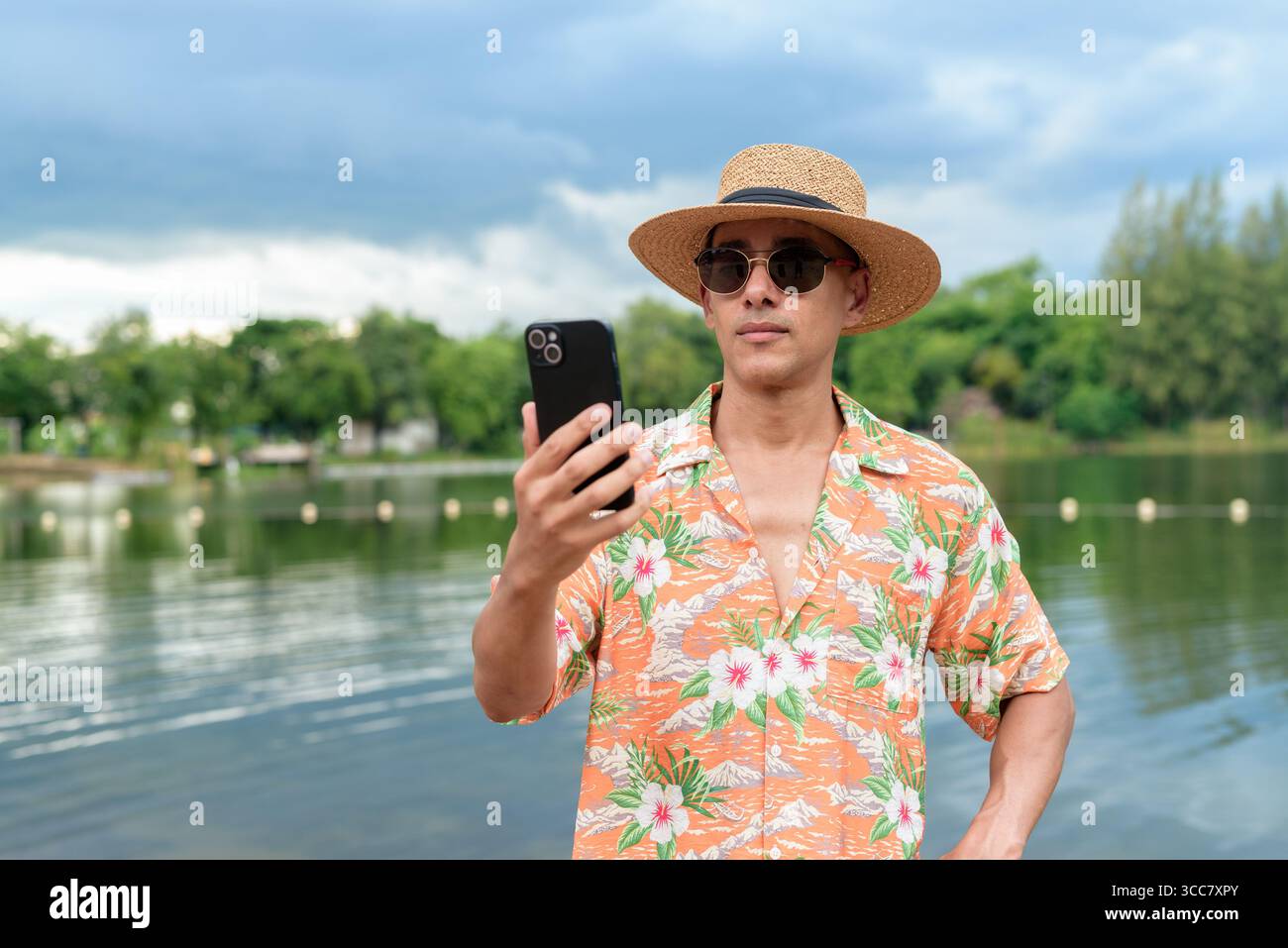 Hispanischer Mann mit Panamahut und hawaiianischem Hemd, gekleidet im lässigen Sommerurlaub-Stil. Er posiert am Strand und zeigt eine entspannte Urlaubsatmosphäre Stockfoto