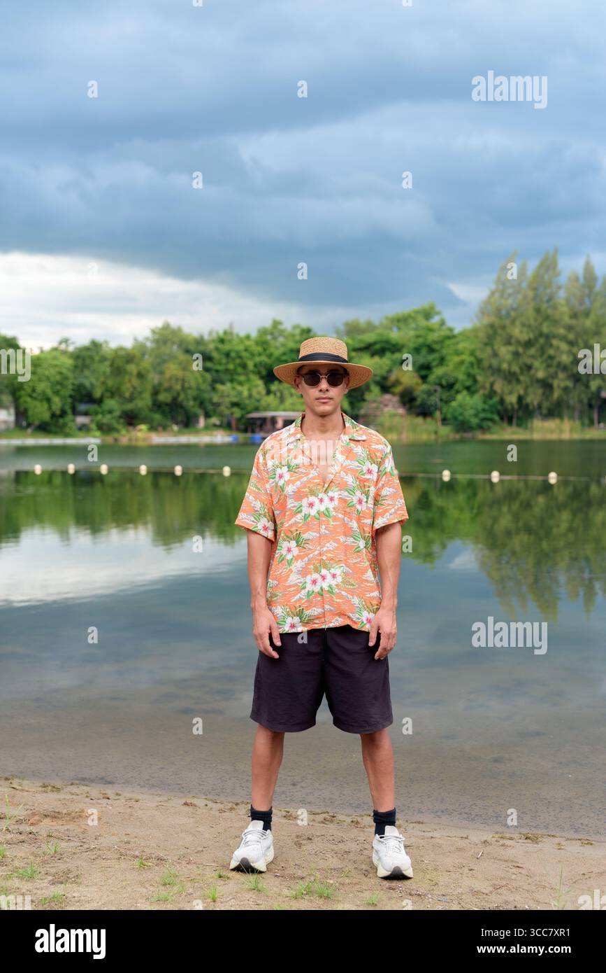 Hispanischer Mann mit Panamahut und hawaiianischem Hemd, gekleidet im lässigen Sommerurlaub-Stil. Er posiert am Strand und zeigt eine entspannte Urlaubsatmosphäre Stockfoto