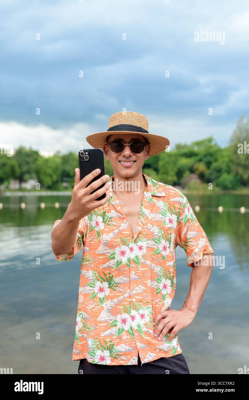 Hispanischer Mann mit Panamahut und hawaiianischem Hemd, gekleidet im lässigen Sommerurlaub-Stil. Er posiert am Strand und zeigt eine entspannte Urlaubsatmosphäre Stockfoto