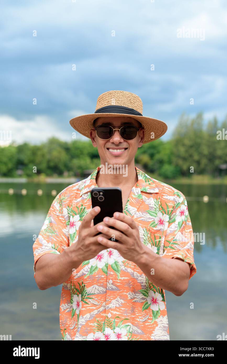 Hispanischer Mann mit Panamahut und hawaiianischem Hemd, gekleidet im lässigen Sommerurlaub-Stil. Er posiert am Strand und zeigt eine entspannte Urlaubsatmosphäre Stockfoto