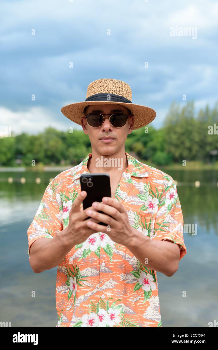 Hispanischer Mann mit Panamahut und hawaiianischem Hemd, gekleidet im lässigen Sommerurlaub-Stil. Er posiert am Strand und zeigt eine entspannte Urlaubsatmosphäre Stockfoto