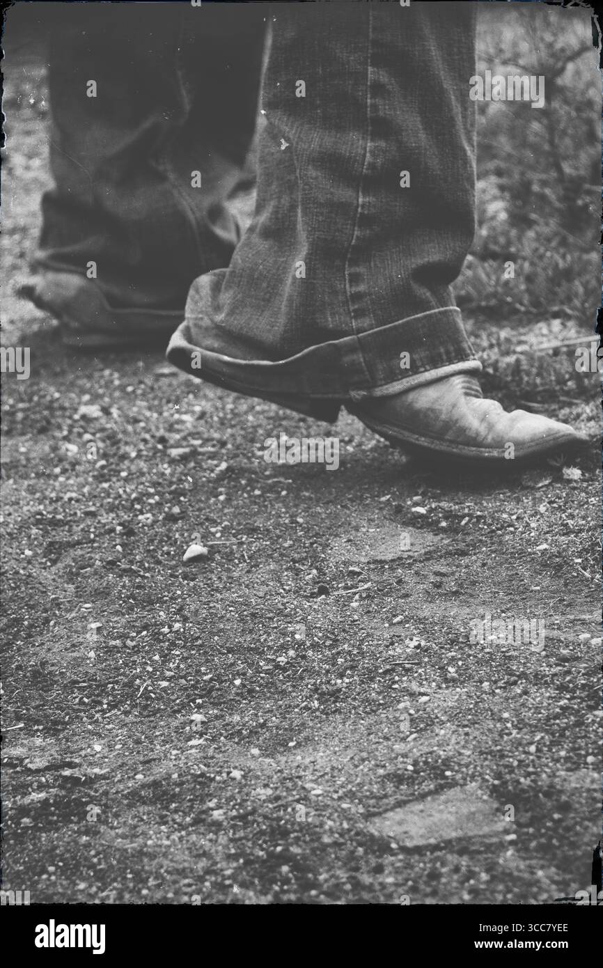 Ein Paar verwitterter Cowboystiefel, Zehen von langen Tagen, schreiten vorwärts über die düstere Erde – ein ruhiges Zeugnis dafür, dass Meilen gelaufen sind und gut gearbeitet haben Stockfoto